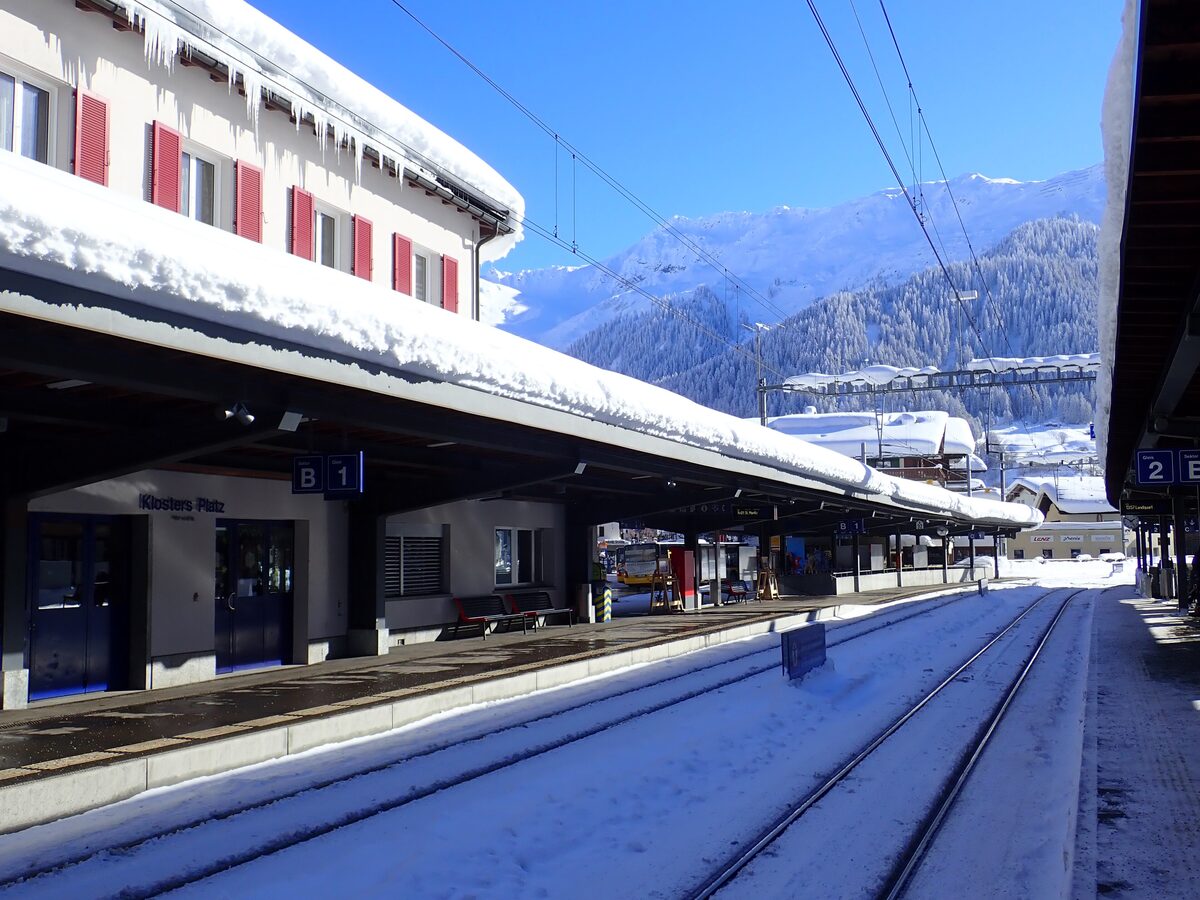 Klosters Platz station in winter, snow and icicles on the platform roof and a snowy ridge behind the tracks