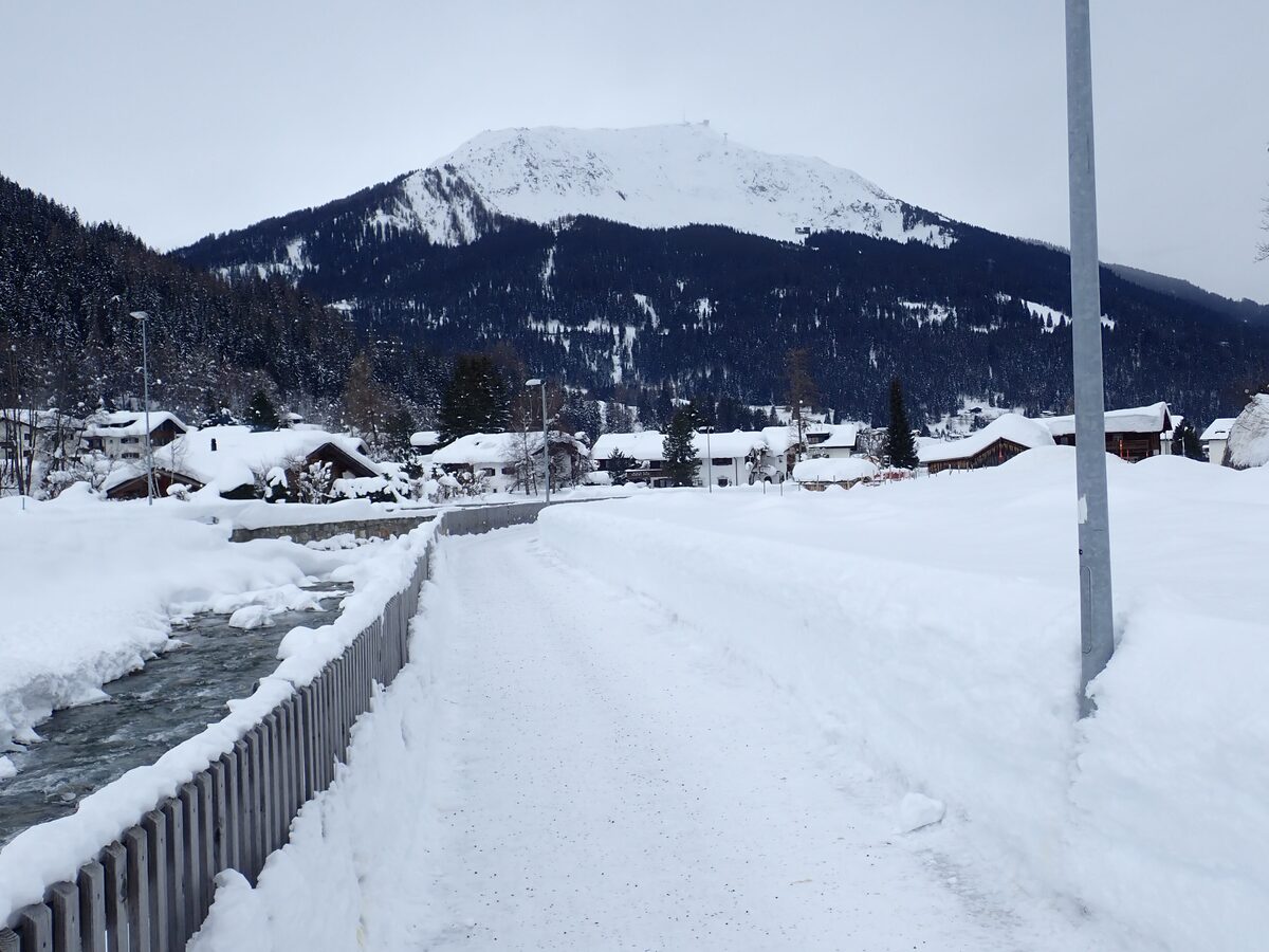 Klosters in deep snow: a cleared path beside a stream, chalets under snowy roofs and a white mountain behind