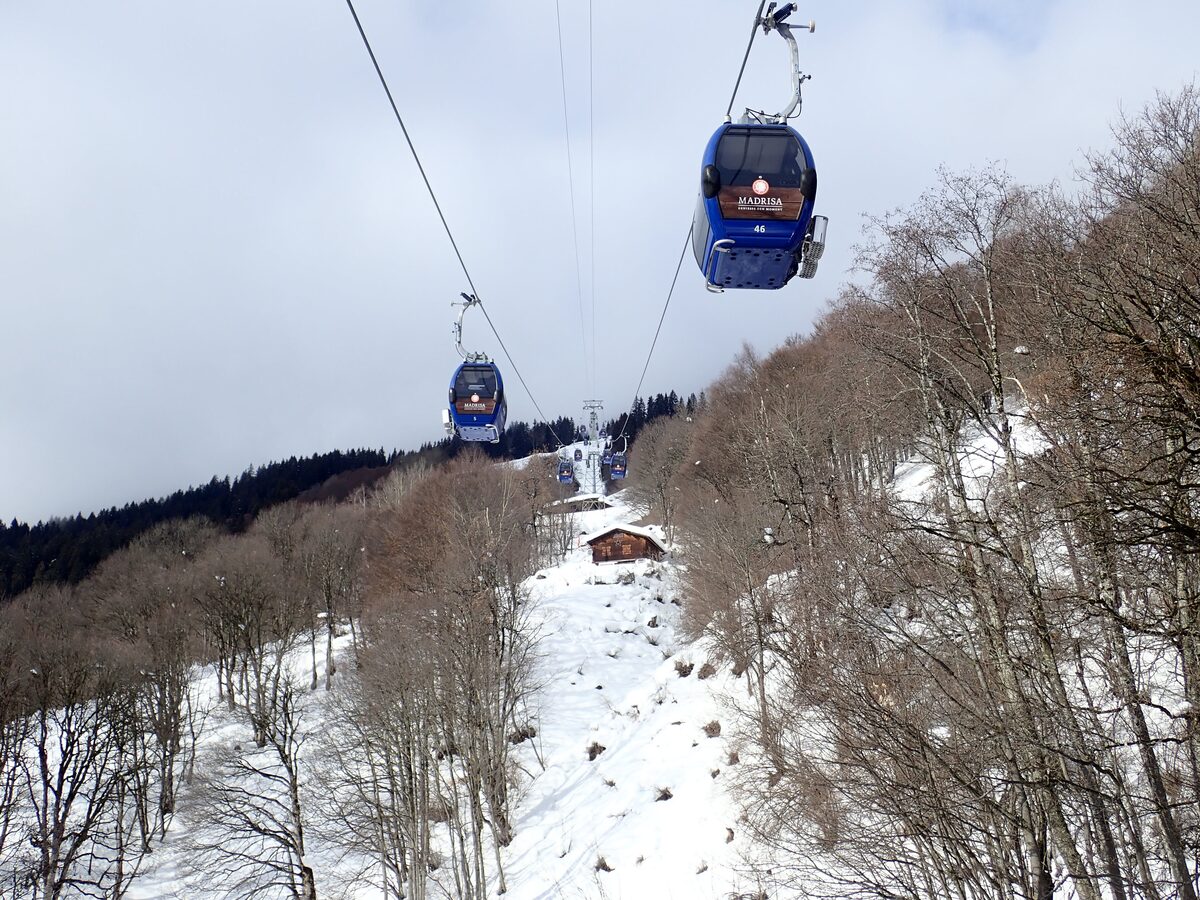 Two blue gondolas of the Klosters-Madrisa cable car above a snowy slope with bare larches