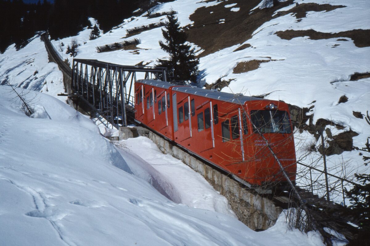 A red Parsenn funicular car standing in deep snow on its track above Davos, in a 1982 photo