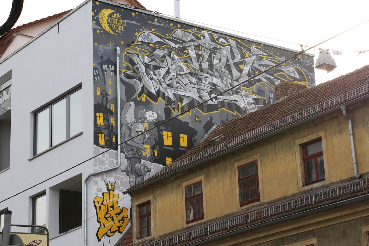 A large graffiti mural on a house wall on Alaunstraße in the Äußere Neustadt, next to an old yellow building