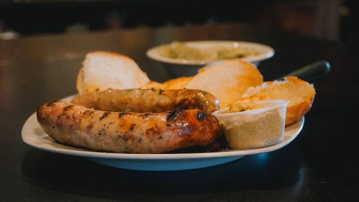 Two grilled bratwursts on a plate with bread rolls and mustard