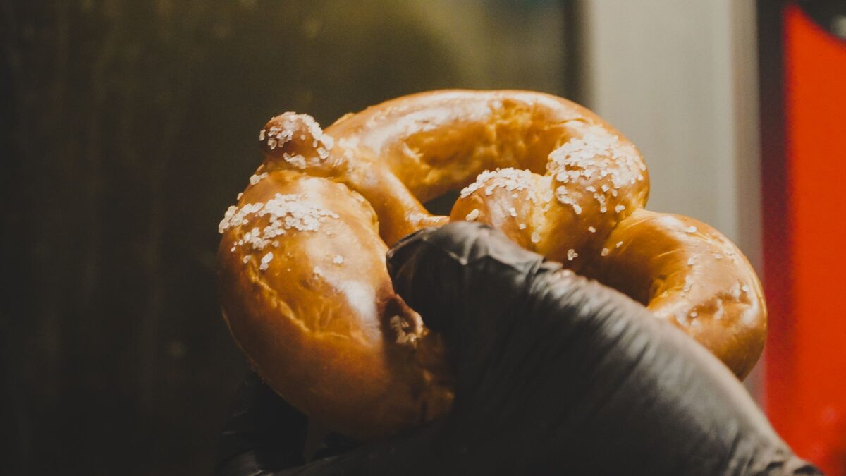 A hand holding a freshly baked pretzel crusted with coarse salt