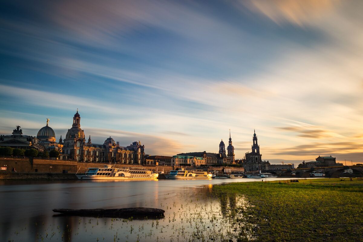 The Altstadt skyline across the Elbe at dusk, with the Frauenkirche dome and the Hofkirche tower under streaky evening clouds