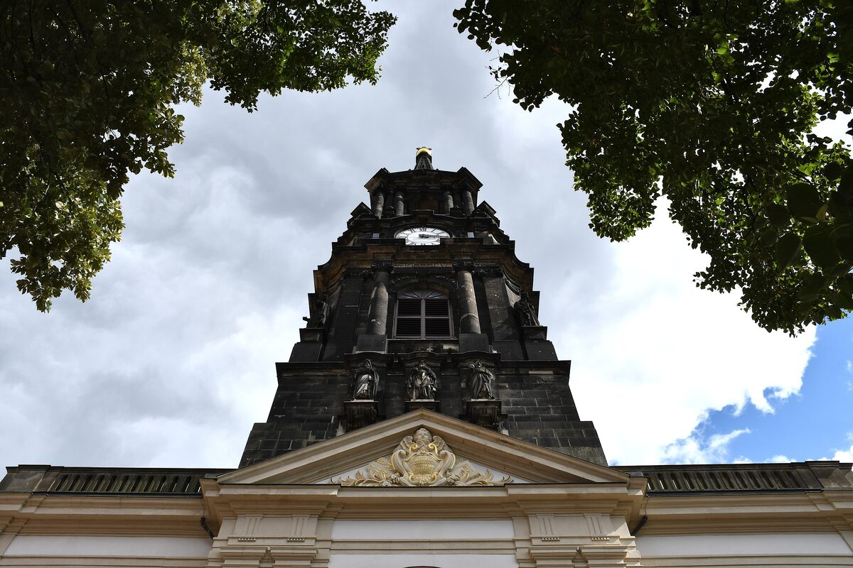 Looking up at the dark tower of the Dreikönigskirche between tree branches and a cloudy sky
