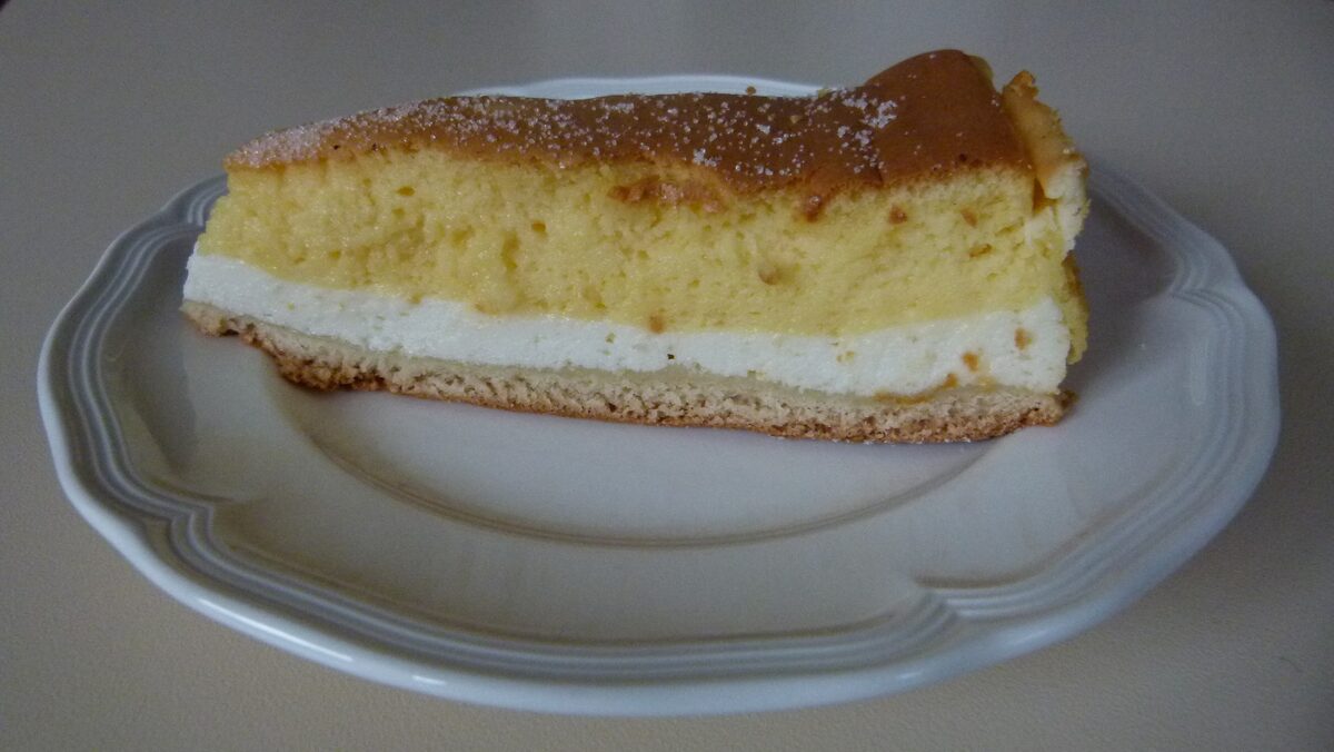 A slice of Eierschecke with a base, a quark layer and a golden egg-cream top on a white plate