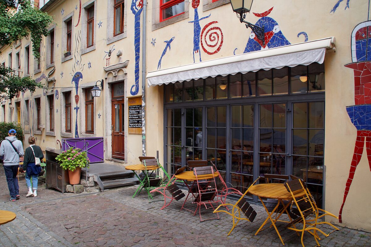 A courtyard in the Kunsthofpassage with mosaic-decorated walls and a café with outdoor tables