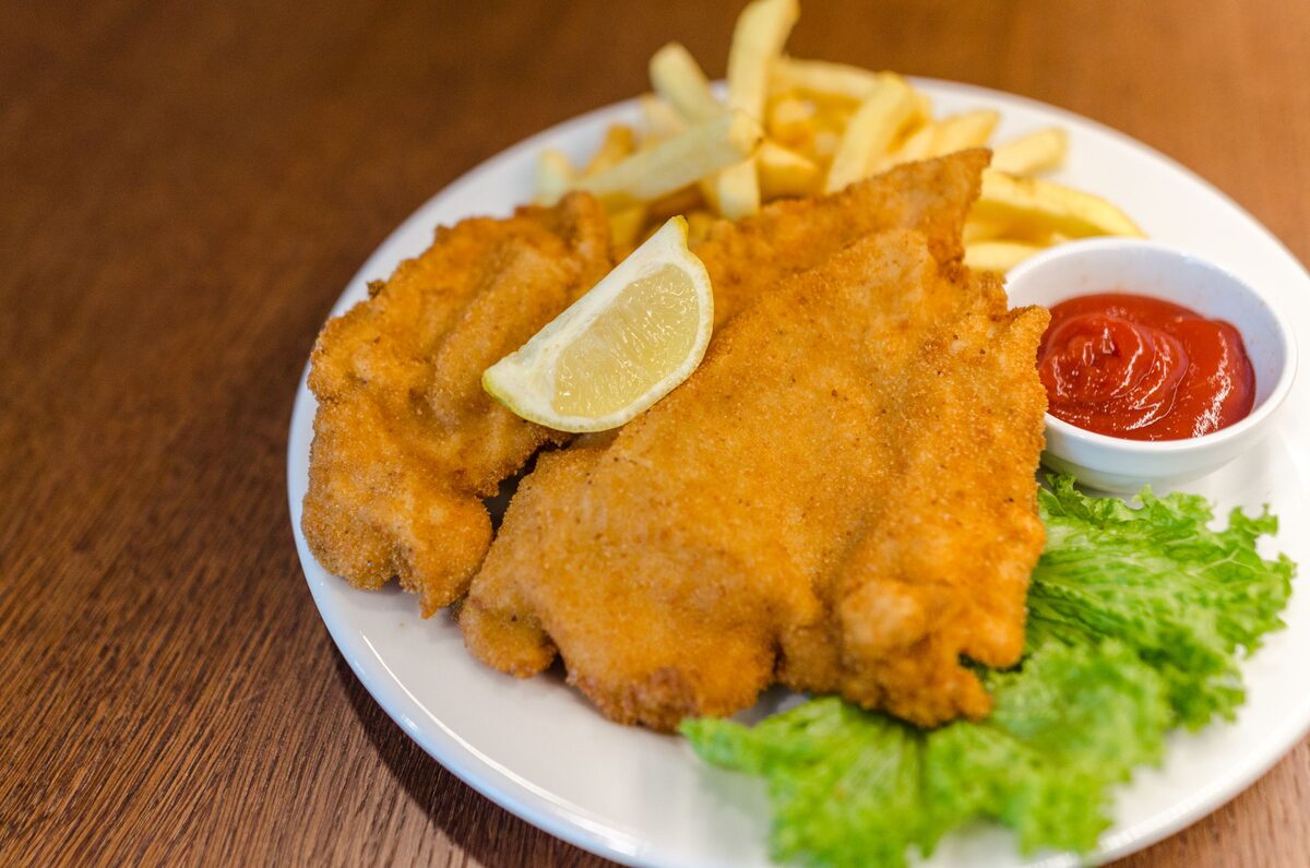 A golden breaded schnitzel with fries, a lemon wedge, ketchup and lettuce