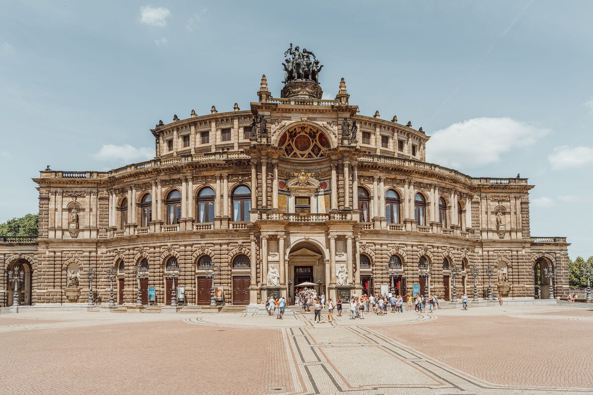 The curved facade of the Semperoper on Theaterplatz, with tourists in front of the main entrance