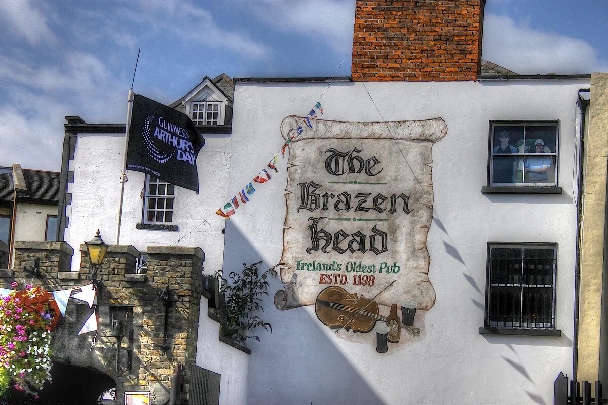 The white front of the Brazen Head pub with its painted sign reading Ireland's Oldest Pub, Estd 1198, and flower baskets by the gate