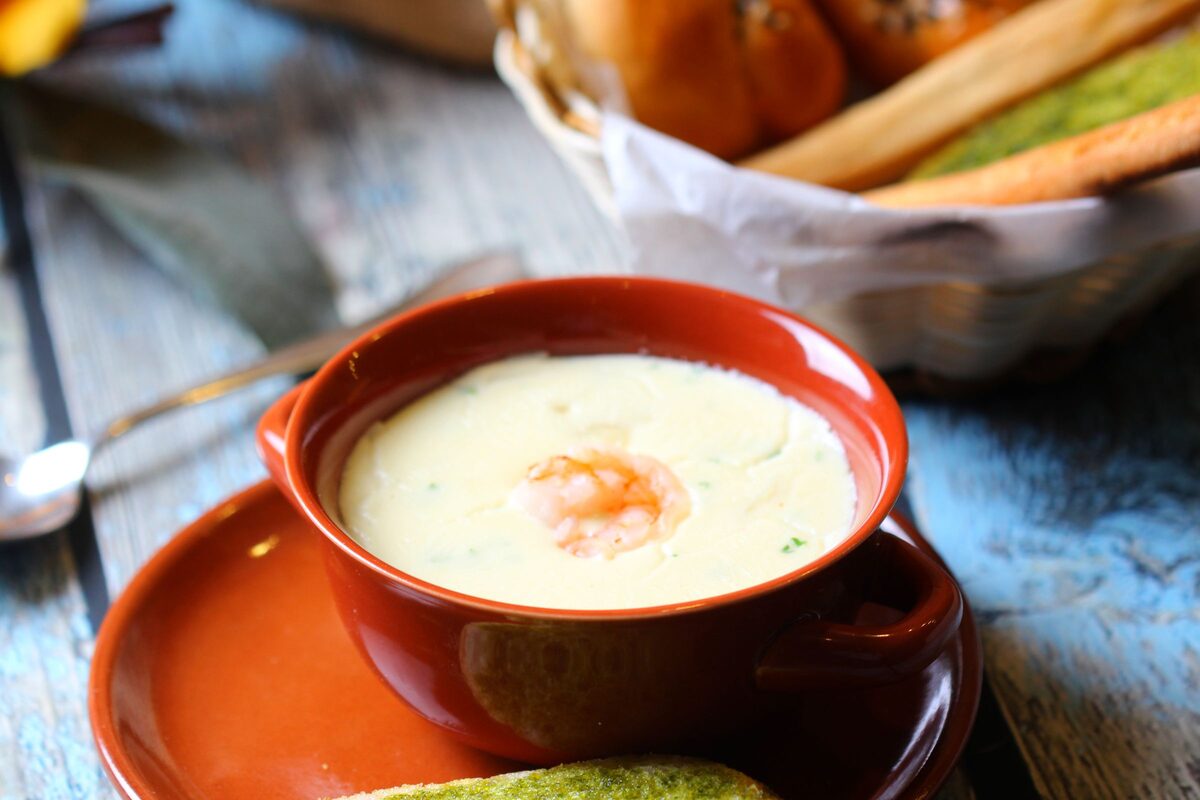 A bowl of creamy seafood chowder topped with a prawn, on a rustic wooden table