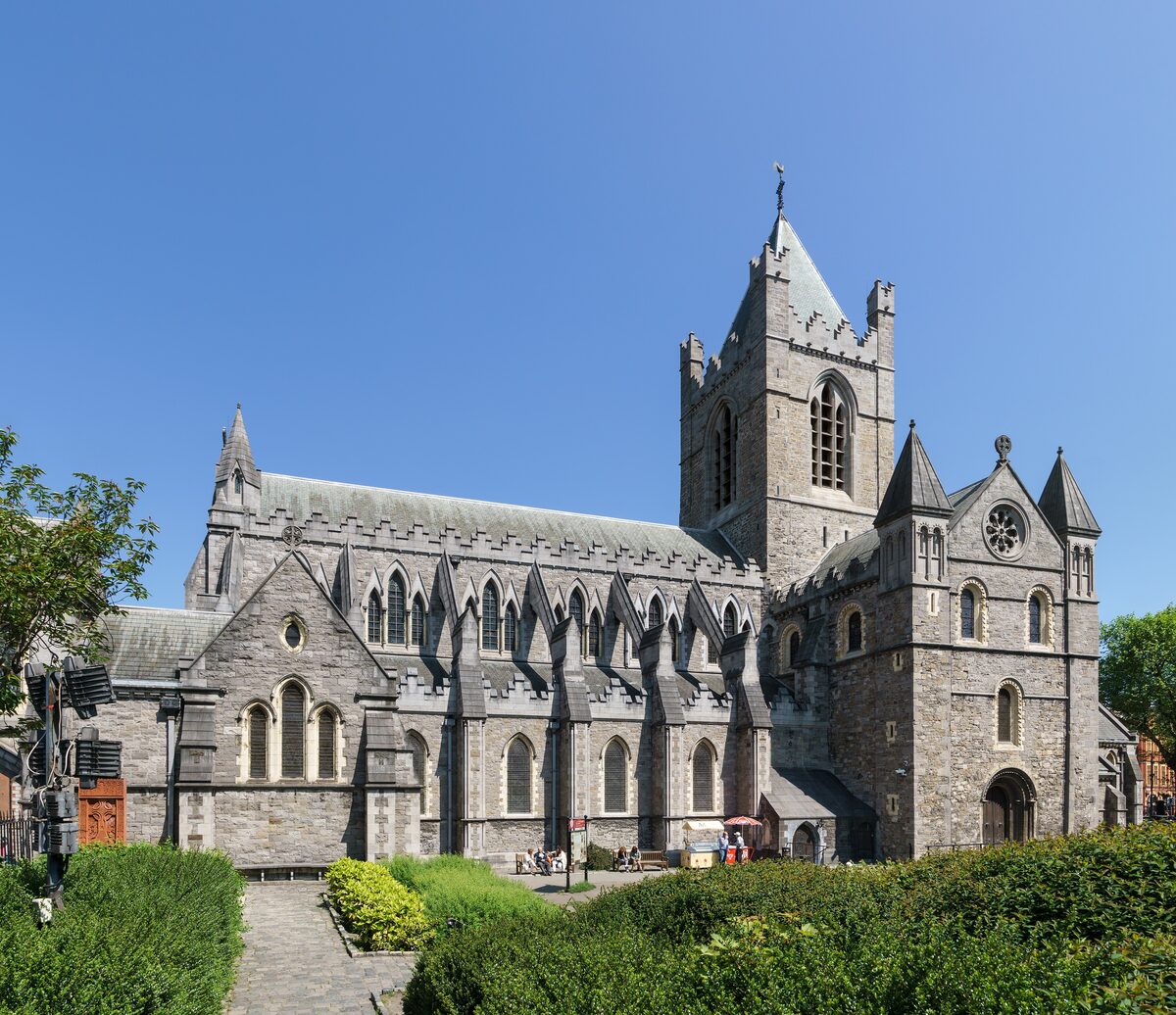 Christ Church Cathedral in Dublin, a gray stone Gothic church with a square tower, flying buttresses and a garden in front, under a blue sky