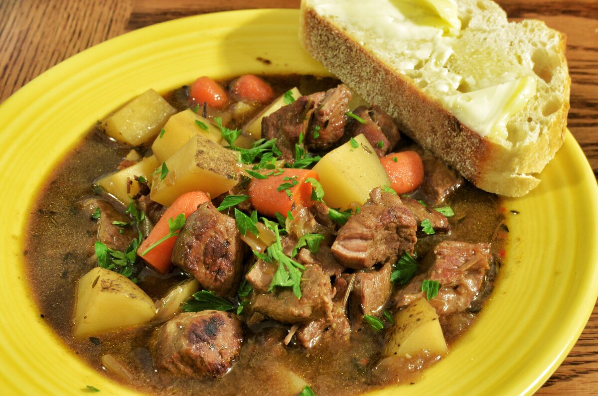 A plate of Irish stew with chunks of lamb, potatoes and carrots in broth, with buttered brown bread on the side