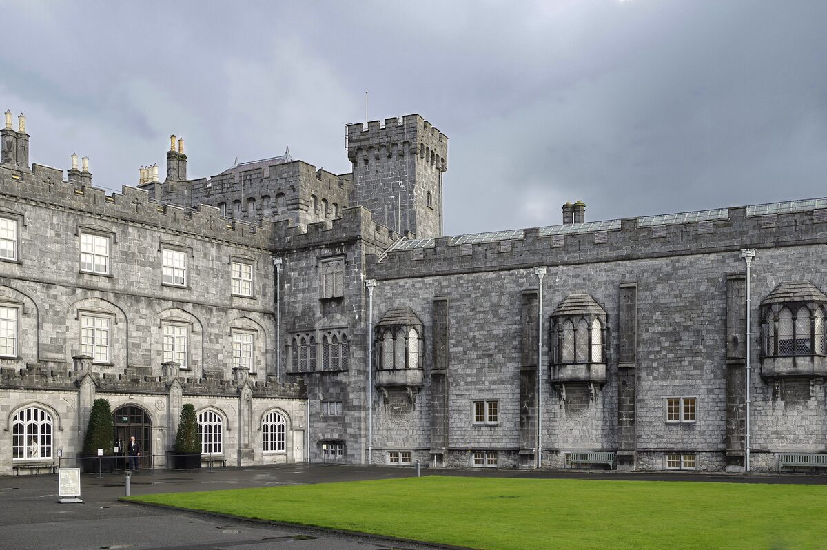 Kilkenny Castle, a large gray stone castle with round towers and battlements, above a lawn
