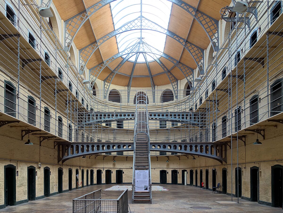 The bright Victorian east wing of Kilmainham Gaol, three floors of cell doors around an open hall under a glass roof, with an iron staircase in the middle