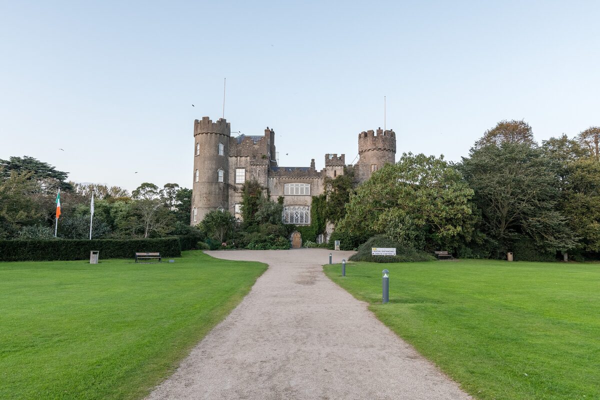 Malahide Castle, a gray stone castle with round towers, at the end of a long path between lawns