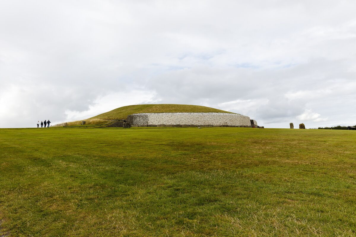 The great round mound of Newgrange with its white quartz front wall, on a green field under a pale sky