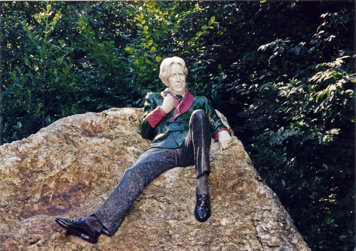 The colorful statue of Oscar Wilde lounging on a large rock in Merrion Square, in a green smoking jacket with a pink collar