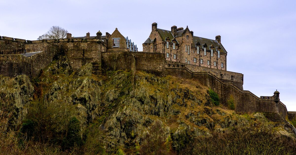 Edinburgh Castle on top of its dark volcanic rock, with buildings along the crag and a pale evening sky