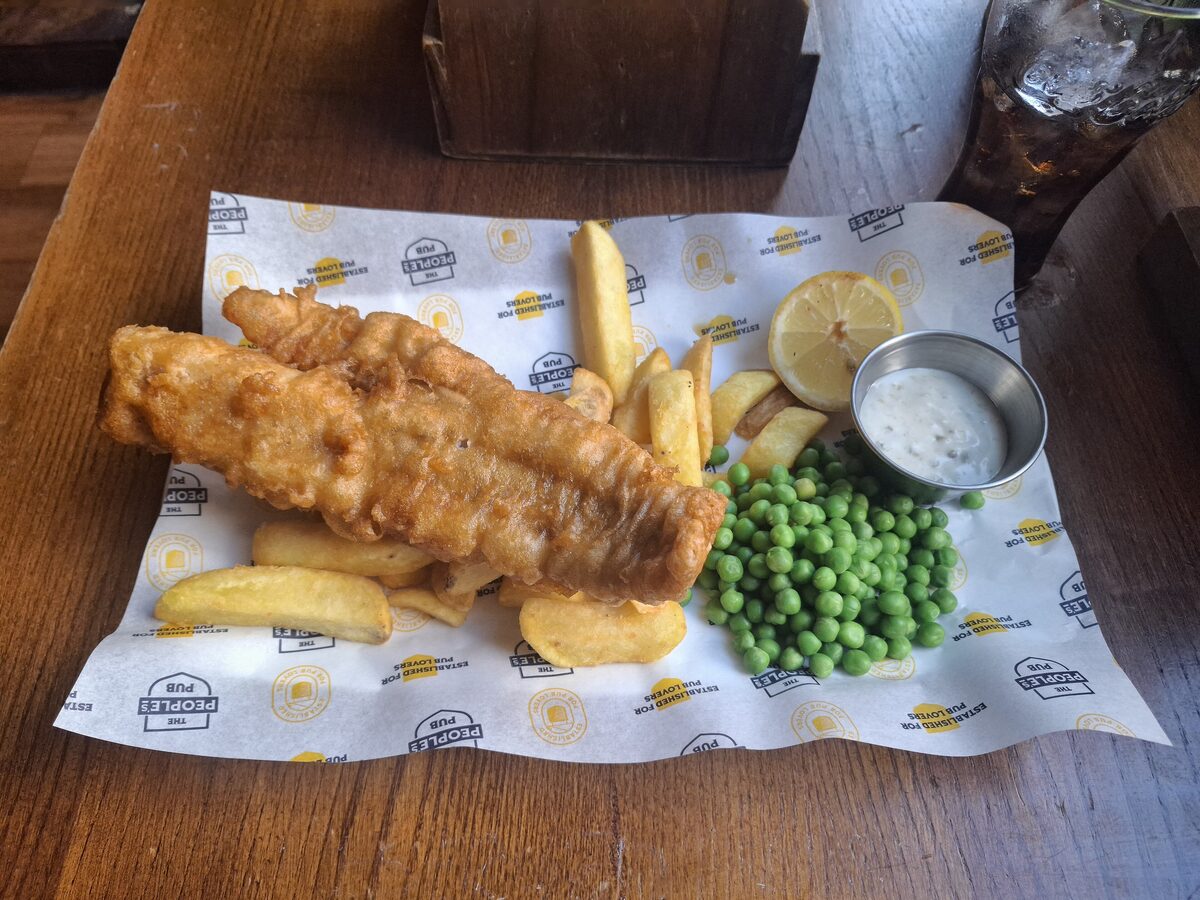Two pieces of battered fish with chips, peas, lemon and tartare sauce on paper in an Edinburgh pub