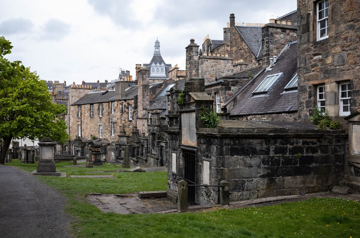 Old gravestones and tombs on the grass of Greyfriars Kirkyard, with tenements of the Old Town behind