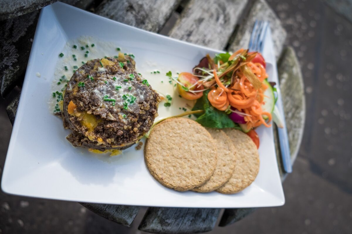 A round of haggis topped with chives on a white plate, with oatcakes and a small salad