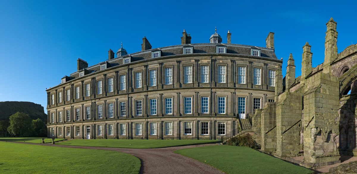 The Palace of Holyroodhouse with its towers and long front, beside the ruined arches of Holyrood Abbey, on a sunny day