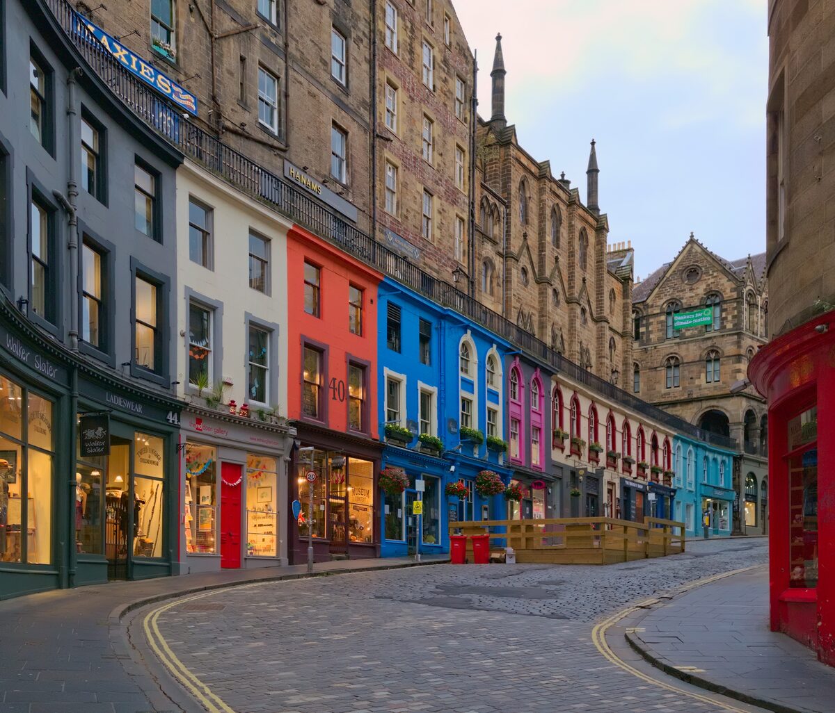 The curving cobbled Victoria Street in Edinburgh, lined with shopfronts painted red, blue and pink