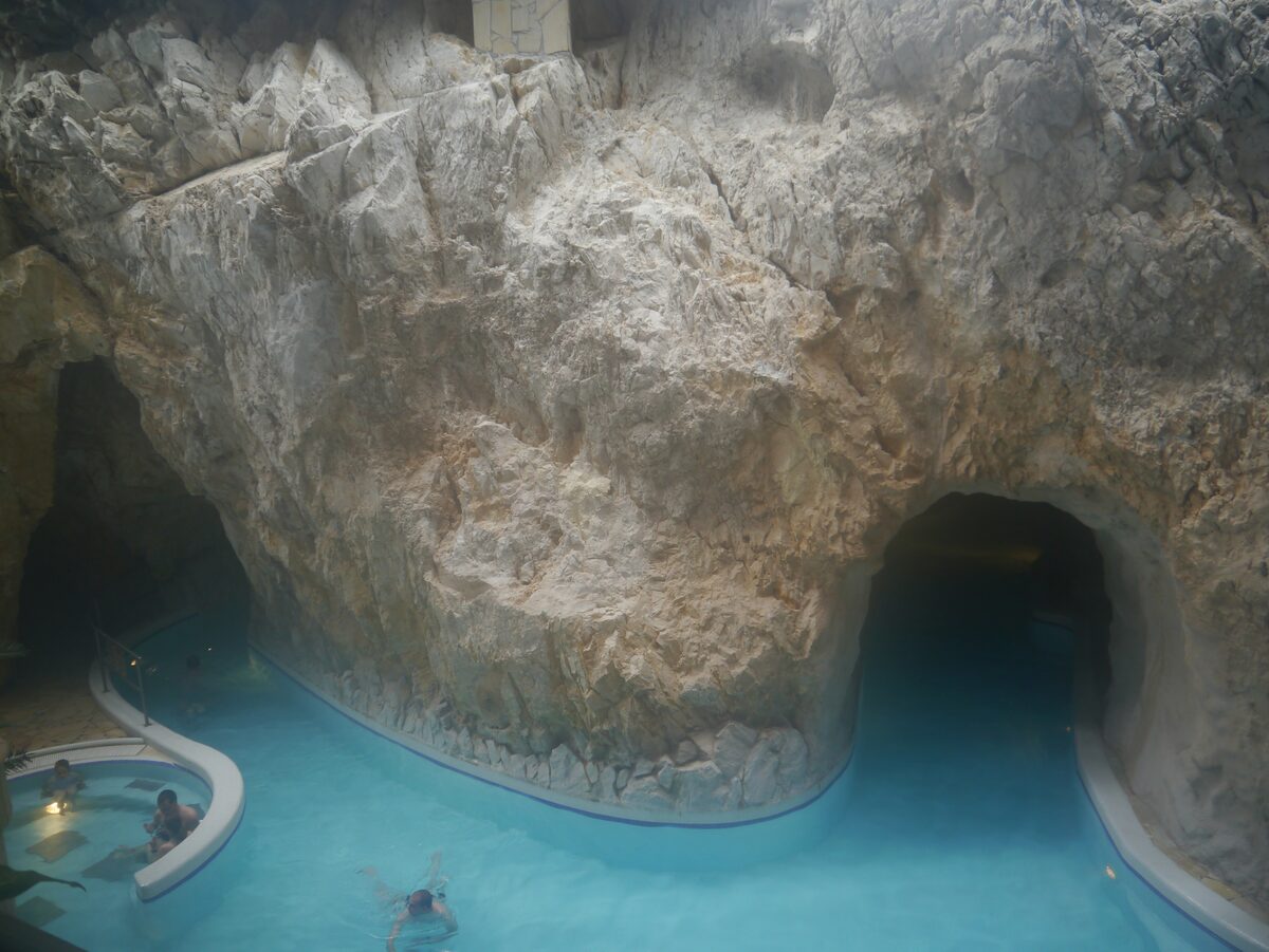 Turquoise thermal water flowing under a pale rock wall into a cave tunnel at the Miskolctapolca Cave Bath