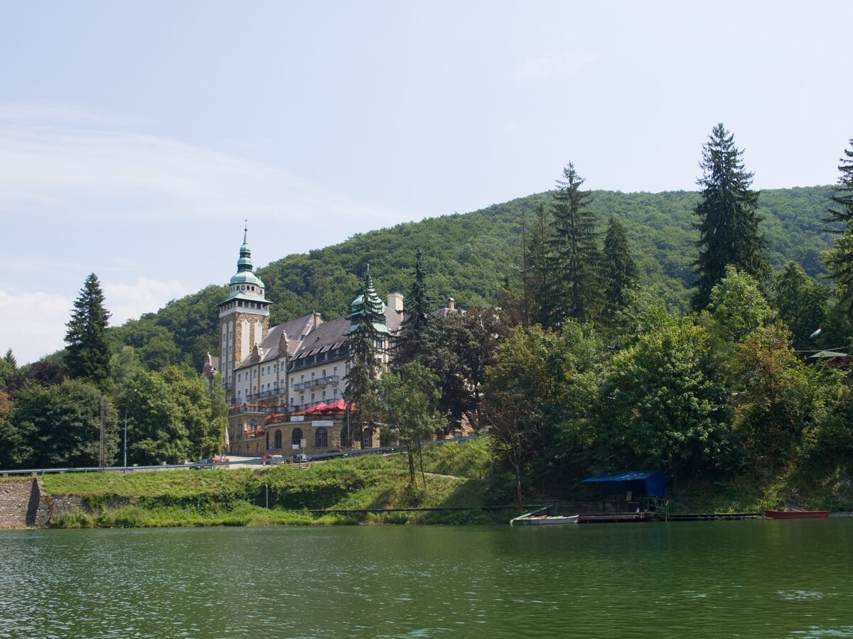 The towered Palace Hotel among wooded hills, seen across the green water of Lake Hámori