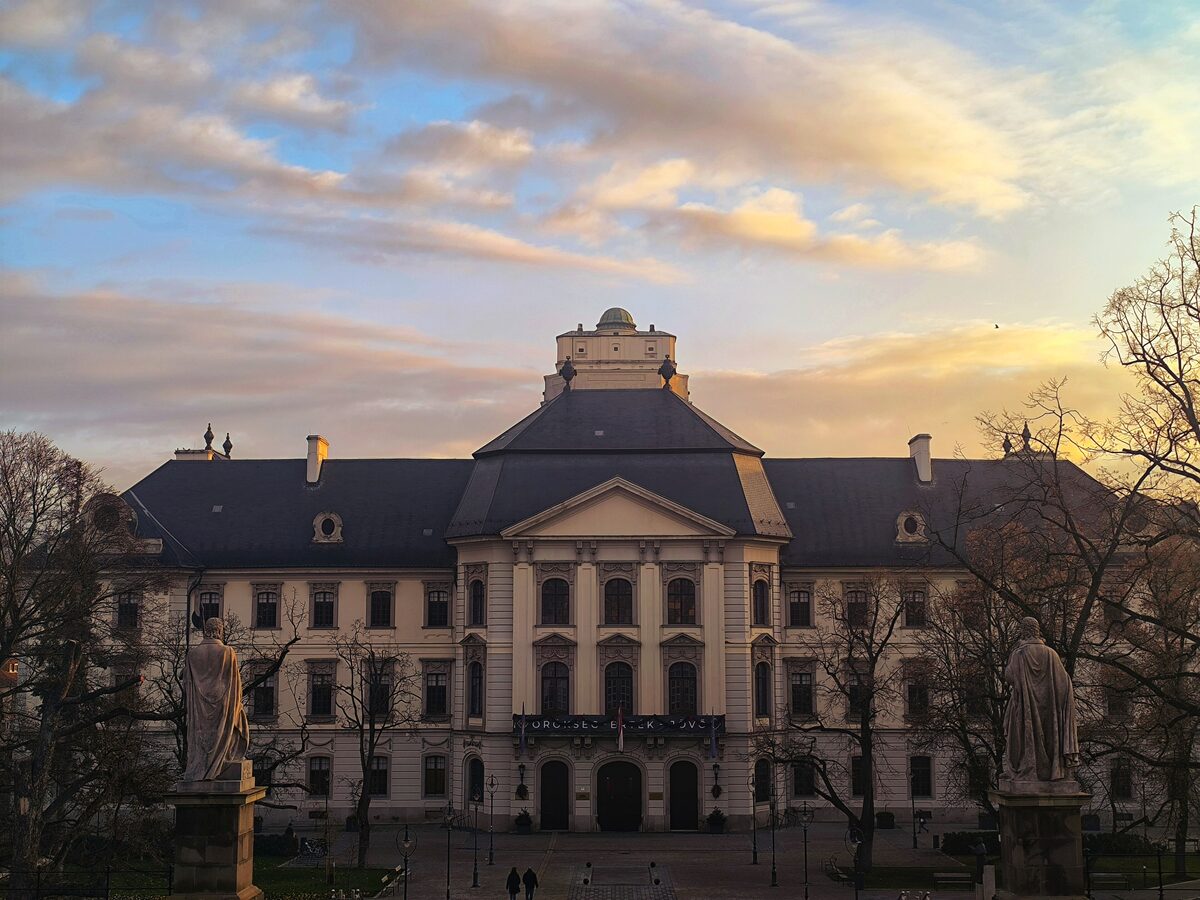 The baroque facade of the Lyceum at sunset, framed by two saint statues from the Basilica steps