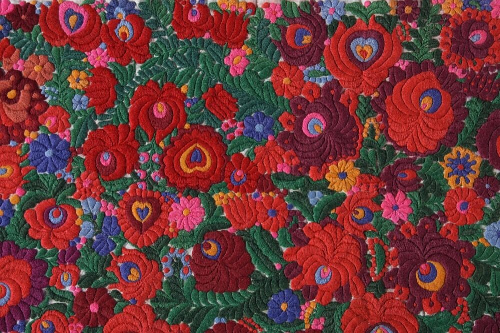 Close-up of dense Matyó embroidery: red, pink and purple roses with green leaves on a wall hanging