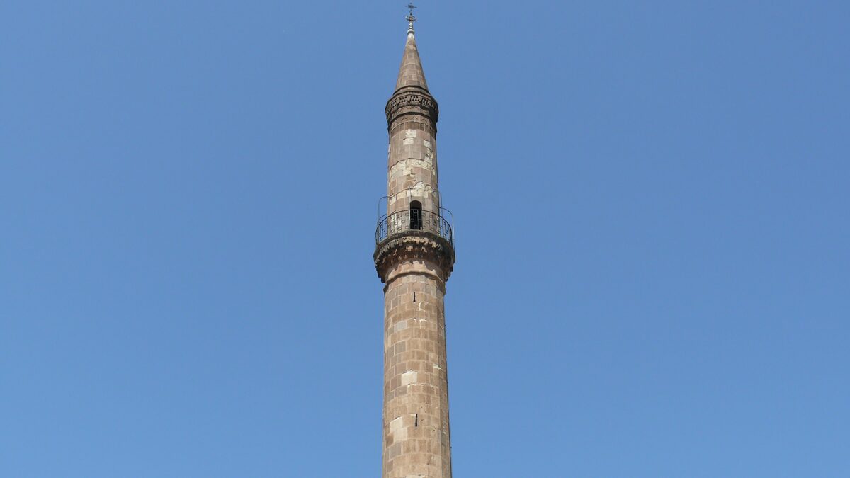 The slender sandstone shaft of the Eger minaret with its railed balcony and pointed cap against a clear blue sky