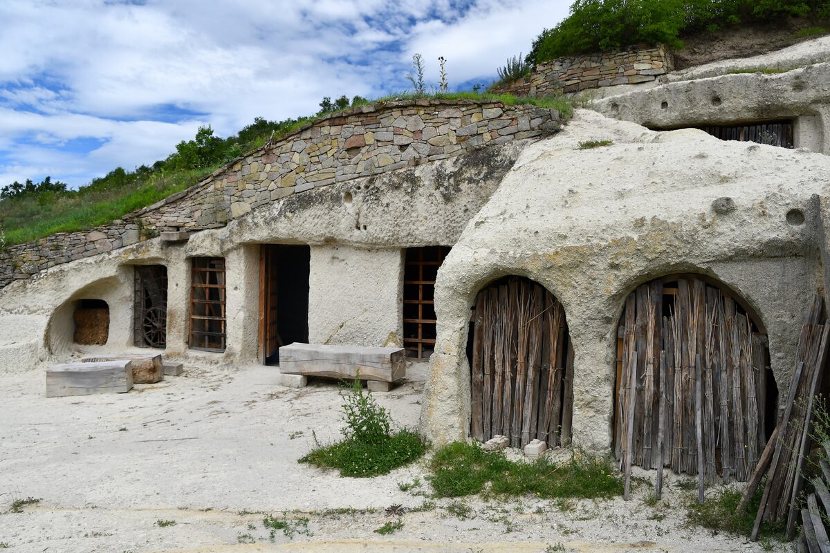 Cave houses carved into pale tuff rock at Noszvaj, with arched wooden doors and small windows