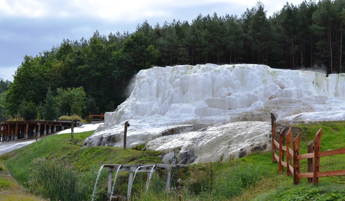 The white travertine terraces of the salt hill at Egerszalók, steaming slightly, in front of a pine forest