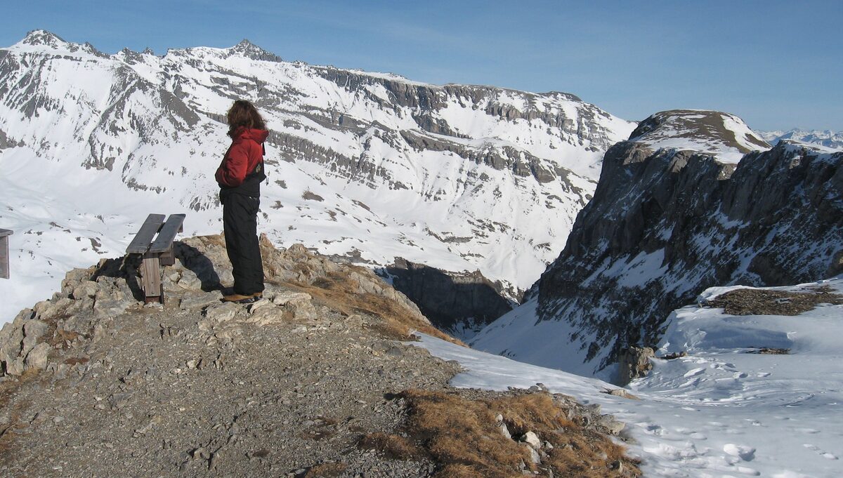 A hiker on a rock outcrop on the snowy Cassons ridge above Flims, with snowy peaks behind