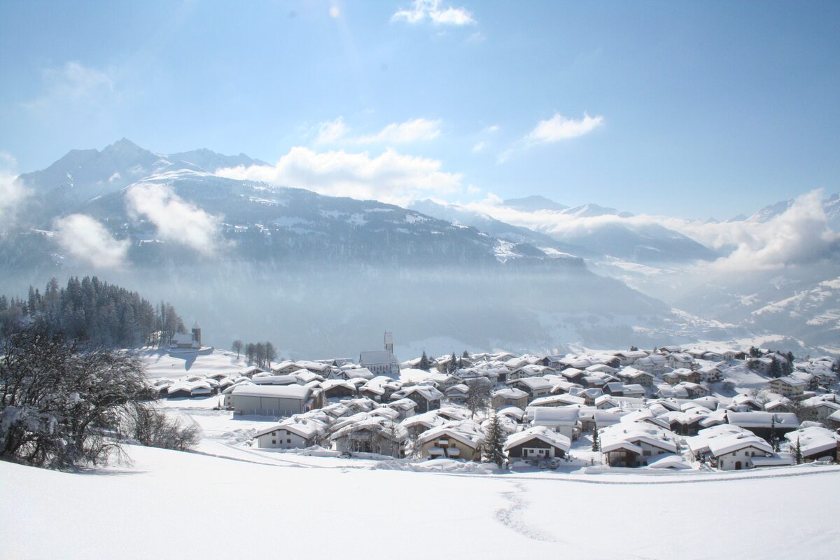 Falera in winter: the village under deep snow, with mountains and cloud beyond