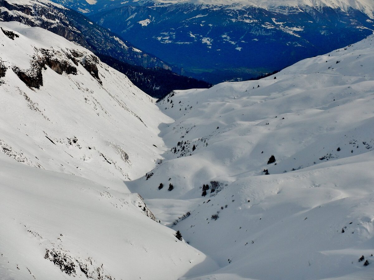 A steep snow valley in the LAAX ski area, with a ridge and the Alps behind