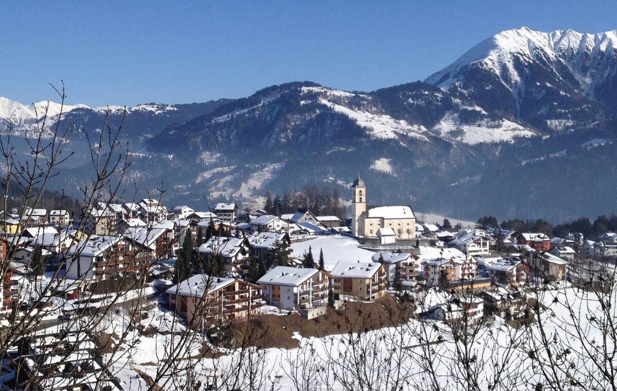 Laax in winter: the village with its church and chalets under snow, with a snowy mountain behind