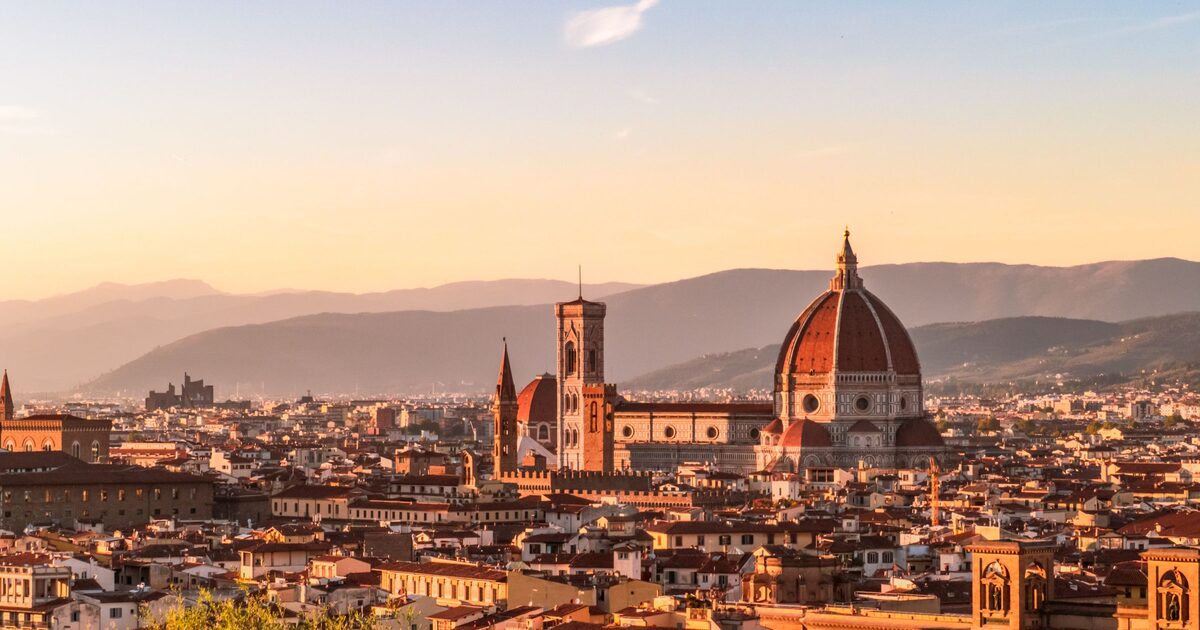 Florence at sunset seen from above, with the red dome of the cathedral, Giotto's bell tower and the old town's rooftops in front of the Tuscan hills
