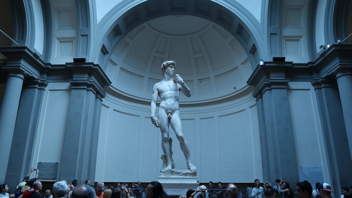 Michelangelo's marble statue of David standing in the rounded tribune of the Accademia, with a crowd of visitors at its base