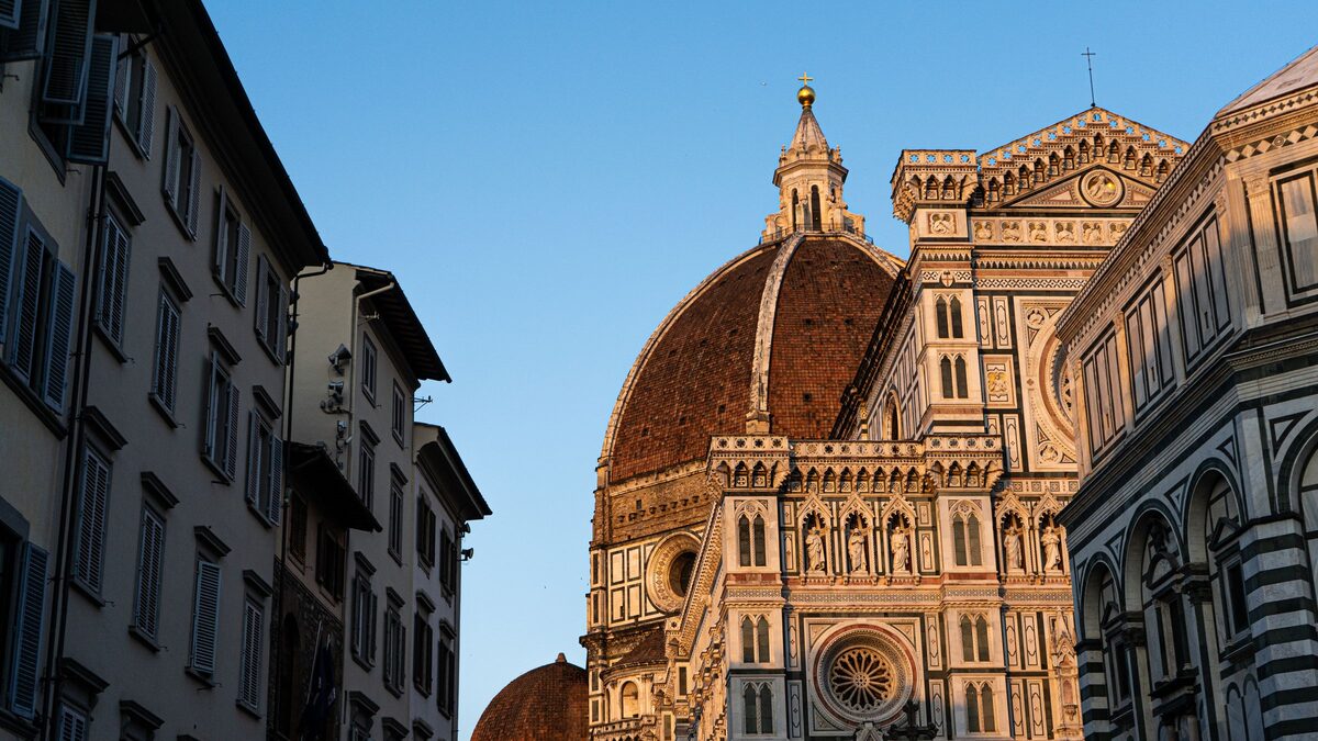 The great red-tiled dome of Florence Cathedral and its marble facade in green, white and pink, glowing in the evening sun between old buildings