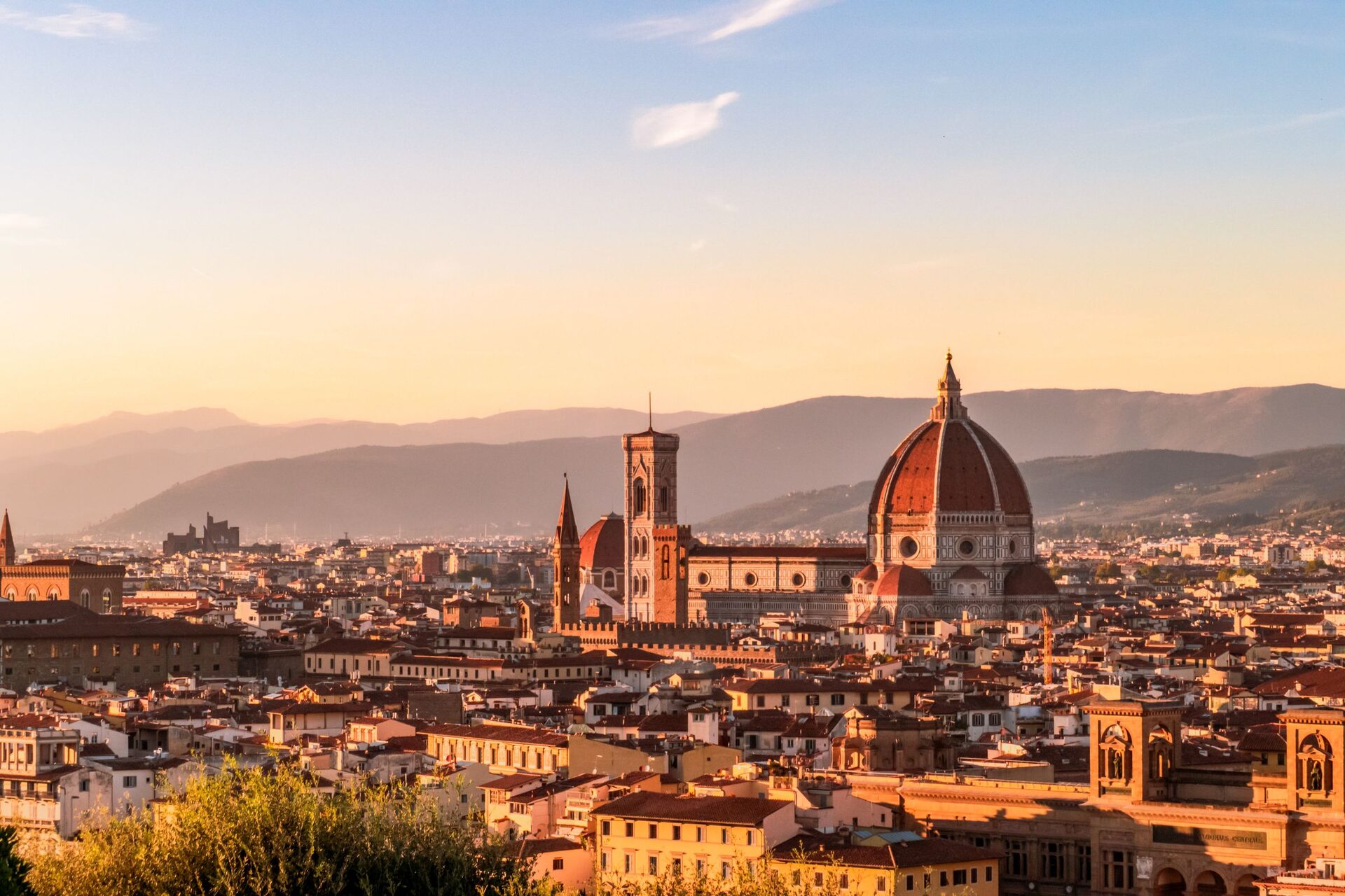 Florence at sunset seen from above, with the red dome of the cathedral, Giotto's bell tower and the old town's rooftops in front of the Tuscan hills