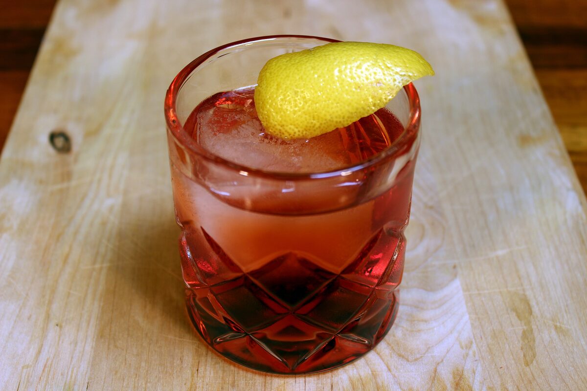 A Negroni cocktail with ice and a slice of lemon in a cut-glass tumbler on a wooden table