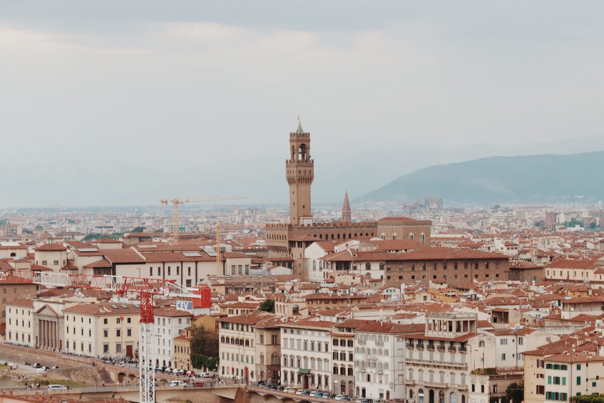 The crenellated tower of Palazzo Vecchio rising above the rooftops of Florence, with green hills behind