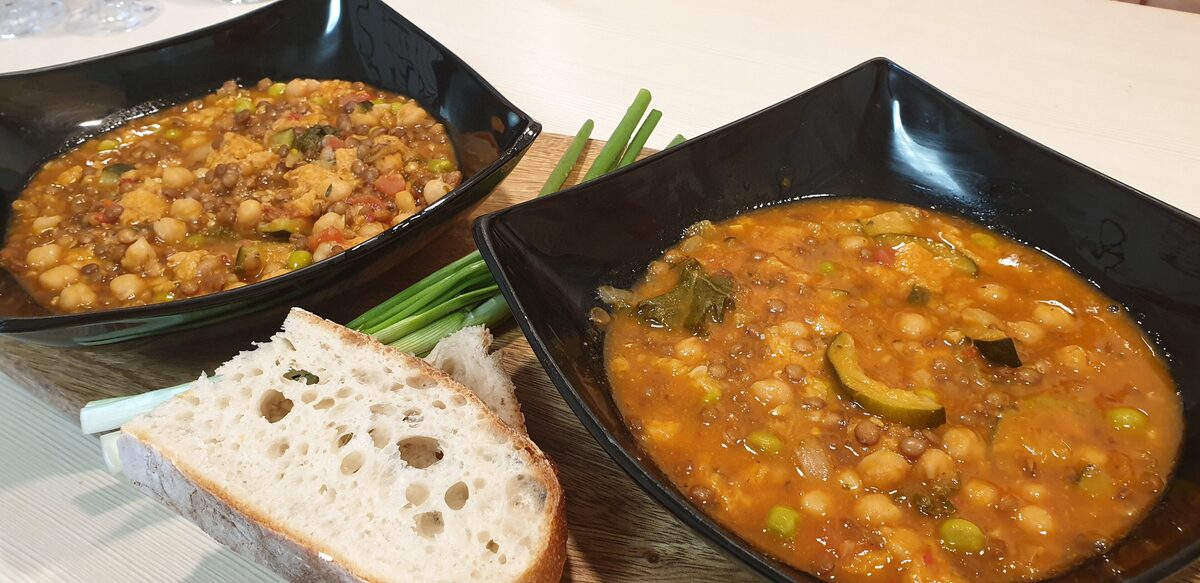 Two bowls of thick Tuscan bean and vegetable soup with slices of rustic bread on the side