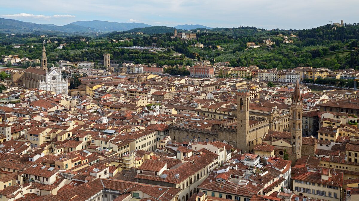 View over the rooftops of Florence to the white marble facade and bell tower of Santa Croce, with green hills behind