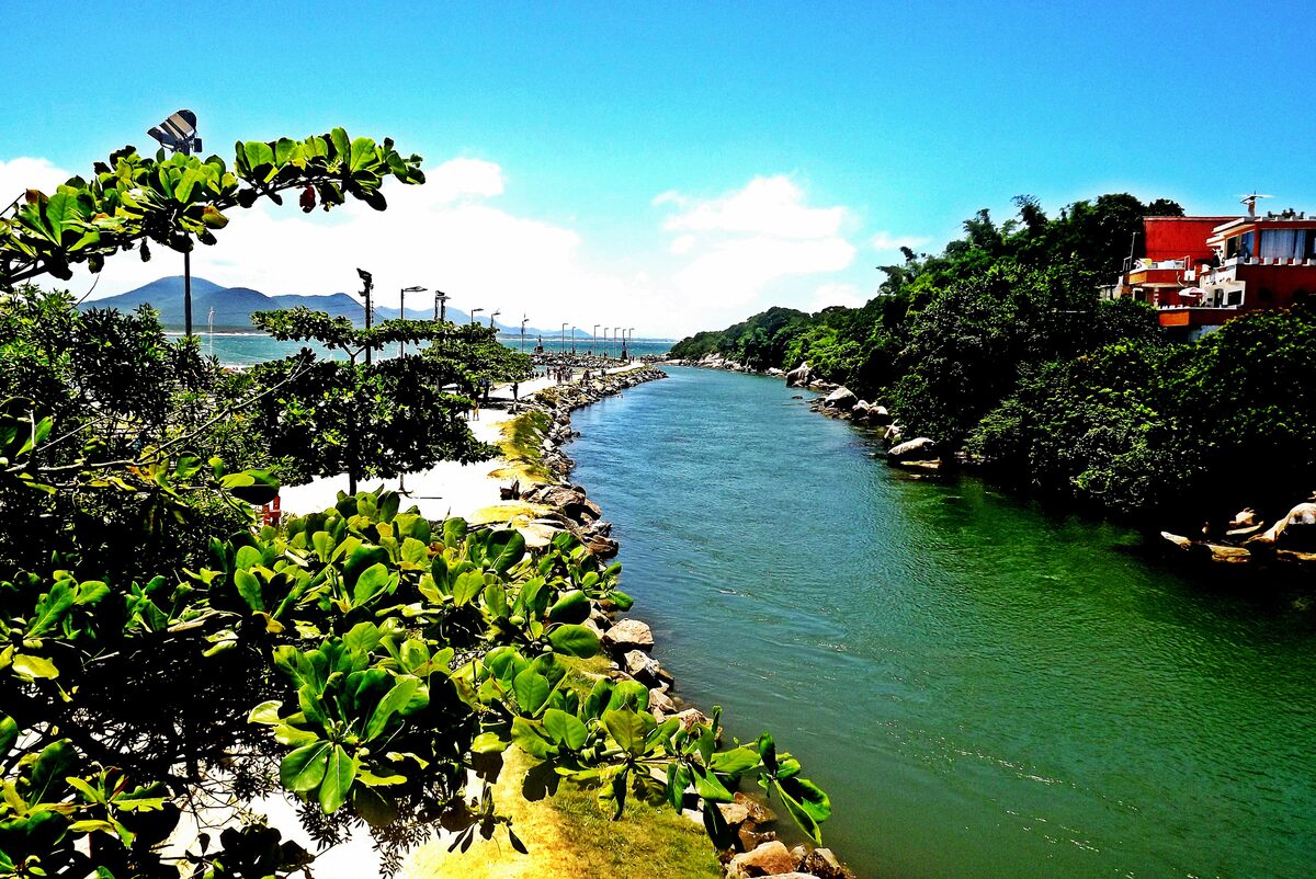 The green canal that links the lagoon to the Atlantic at Barra da Lagoa, with a stone-lined bank and a promenade leading to the sea