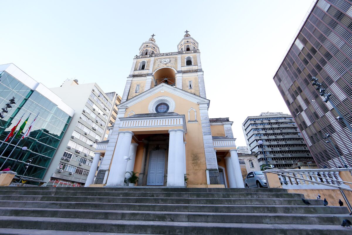 The yellow Catedral Metropolitana facade with twin towers and steps, with modern office towers beside it