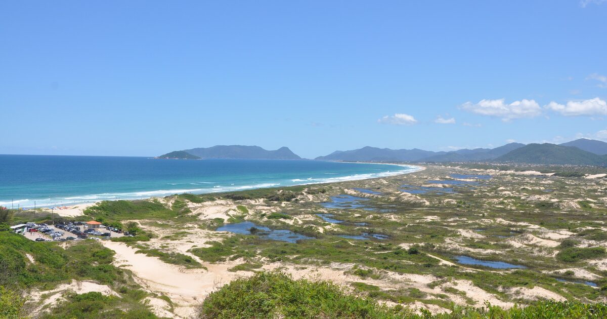 Dune ponds and bare sand above Joaquina beach, with the open Atlantic and islands on the horizon in bright sunshine
